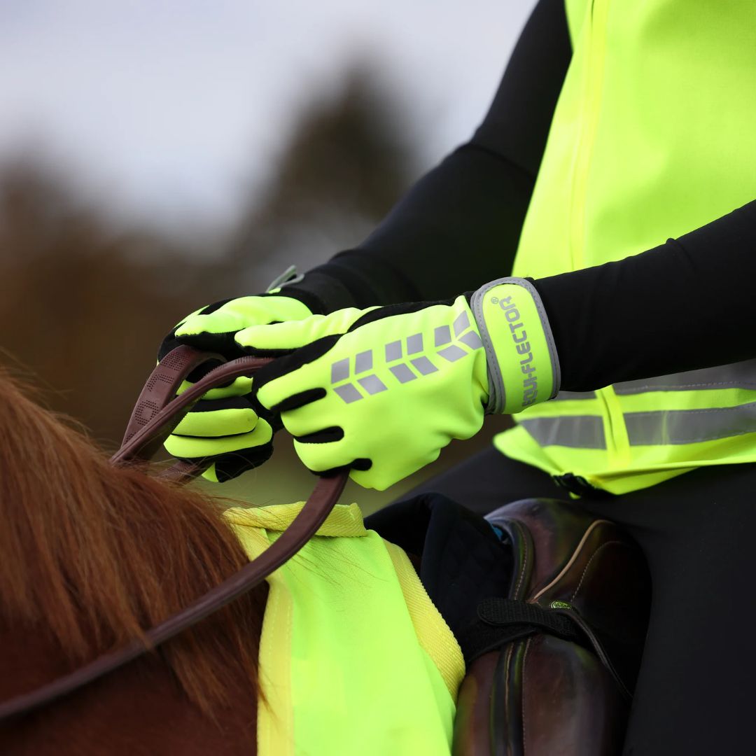 Person wearing bright yellow gloves and a reflective vest interacting with a horse.