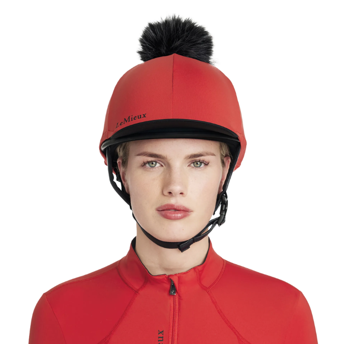 Person wearing a red equestrian helmet with a black pom-pom on a white background