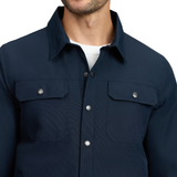 LeMieux AW26 Mens Showerproof Shacket Varient Navy. A close-up of a man wearing a dark navy blue button-up shirt jacket with two chest flap pockets and silver snap buttons, layered over a white t-shirt.