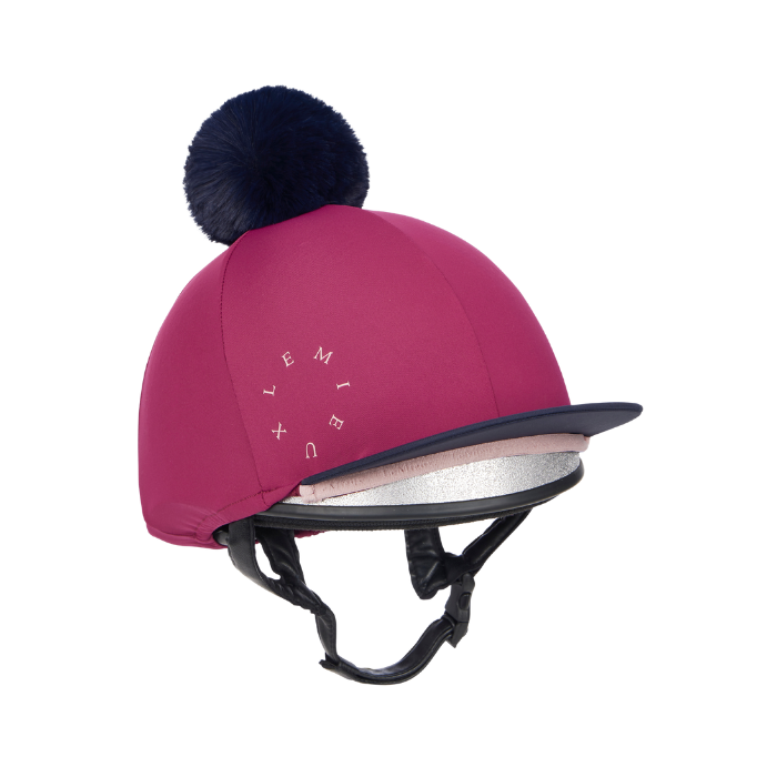 LeMieux AW26 Classique Pom Hat Silk Variant Colour Blackberry.
A blackberry pink equestrian riding helmet cover with a dark navy blue pom-pom on top, featuring the brand name 'LEMIEUX' in white text on the side and a black visor.