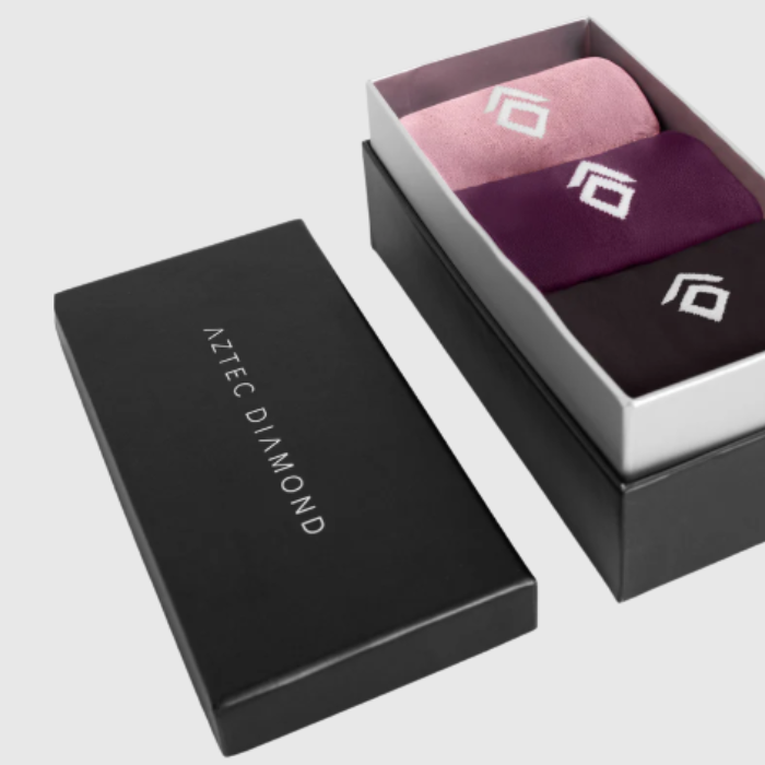 Three pairs of pink, plum and expresso socks in a 'Aztec Diamond' branded box on a light gray background.