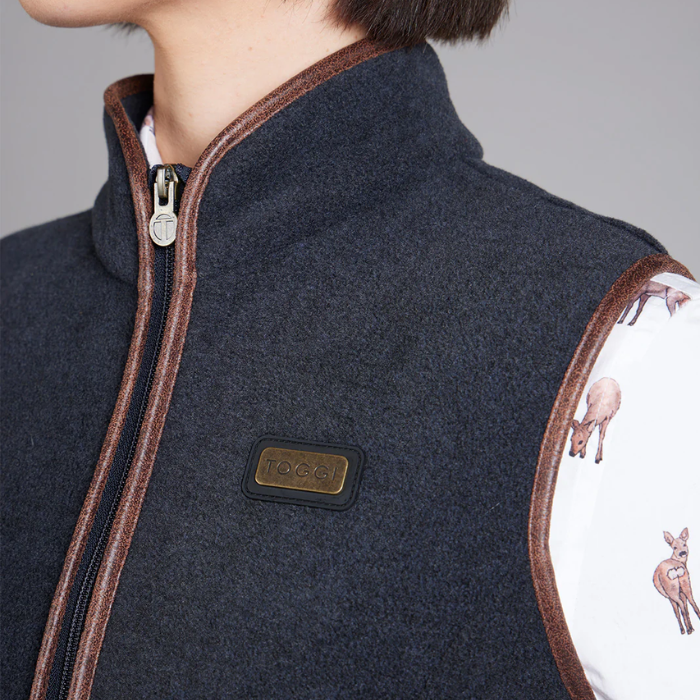 Close-up of a navy blue gilet with brown trim and a brand logo, worn by a person.