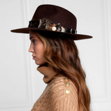 Woman wearing a brown hat with feather accents and a beige cable knit sweater against a white background