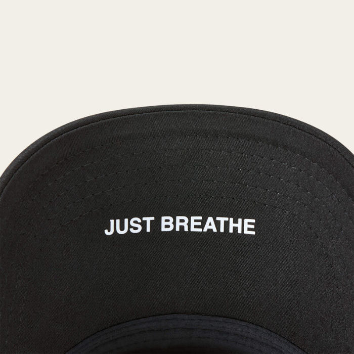 Under rim of black baseball cap with 'Just Breathe' in white writing on white background