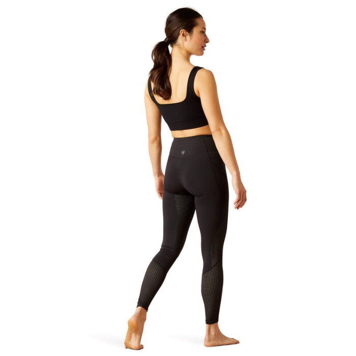 Woman wearing black athletic leggings and sports bra on a white background