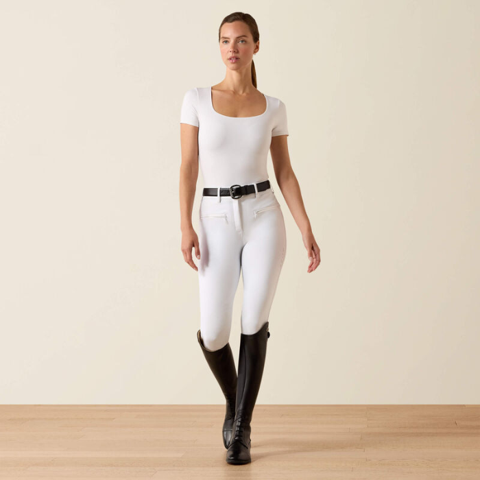Woman wears white riding breeches, t-shirt and black riding boots on a beige background