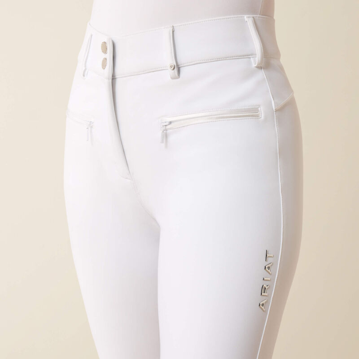 Pair of white riding breeches with ARIAT logo on a beige background