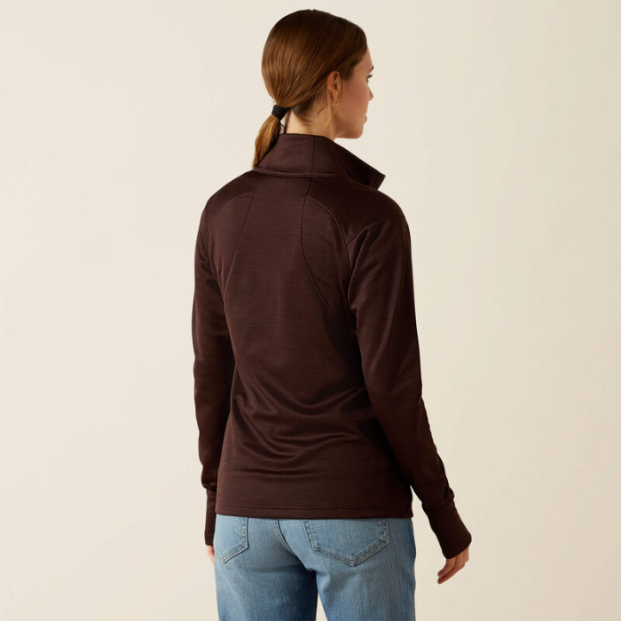 Woman wearing a brown long-sleeve top and blue jeans on a beige background