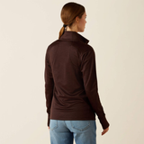 Woman wearing a brown long-sleeve top and blue jeans on a beige background