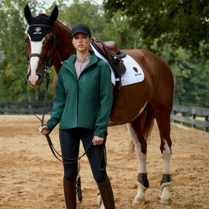Woman in equestrian attire standing next to a horse in an outdoor setting