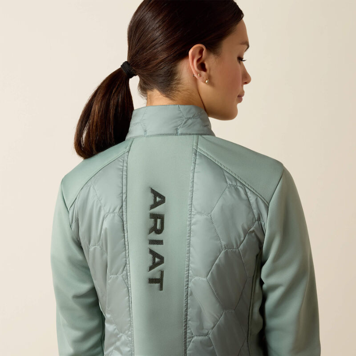 Person wearing a light green quilted jacket with 'Ariat' branding on the back, against a beige background.