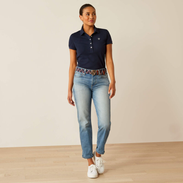 Woman wearing a navy polo shirt, light blue jeans, and white training shoes on a plain background