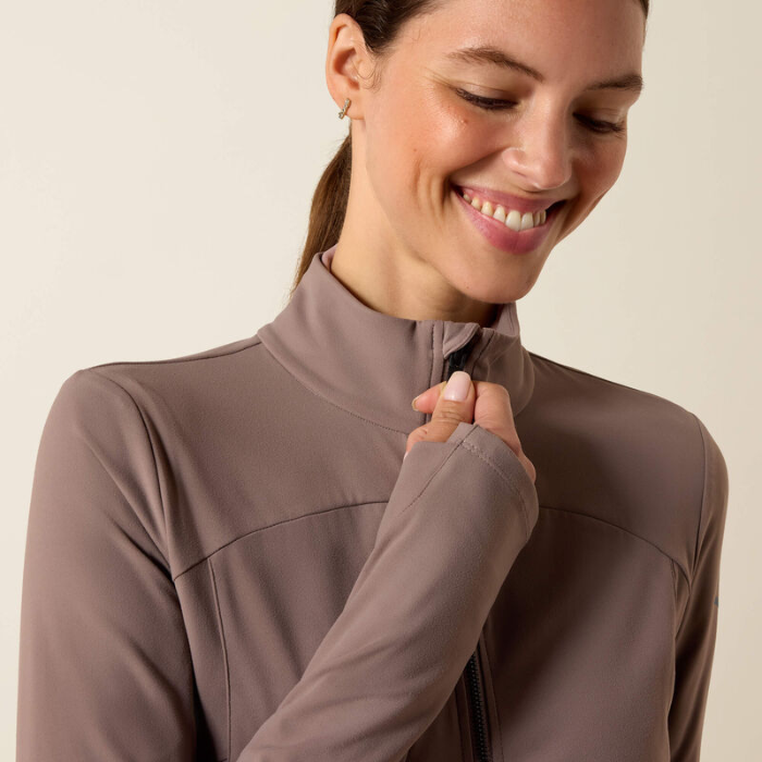 Woman wears a brown full zip jacket against a beige background