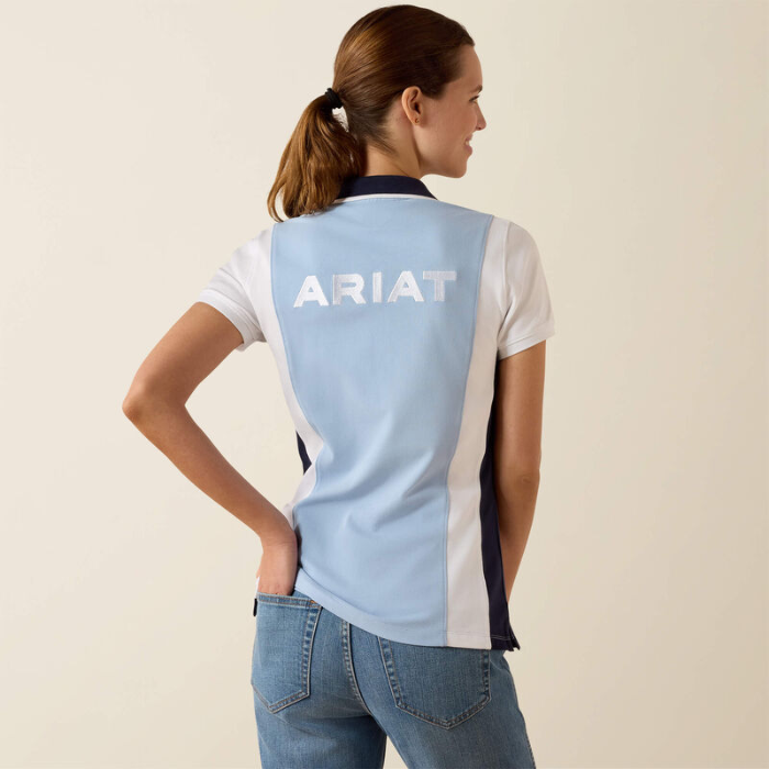 Woman wears a blue and white polo shirt with ARIAT logo on a plain background