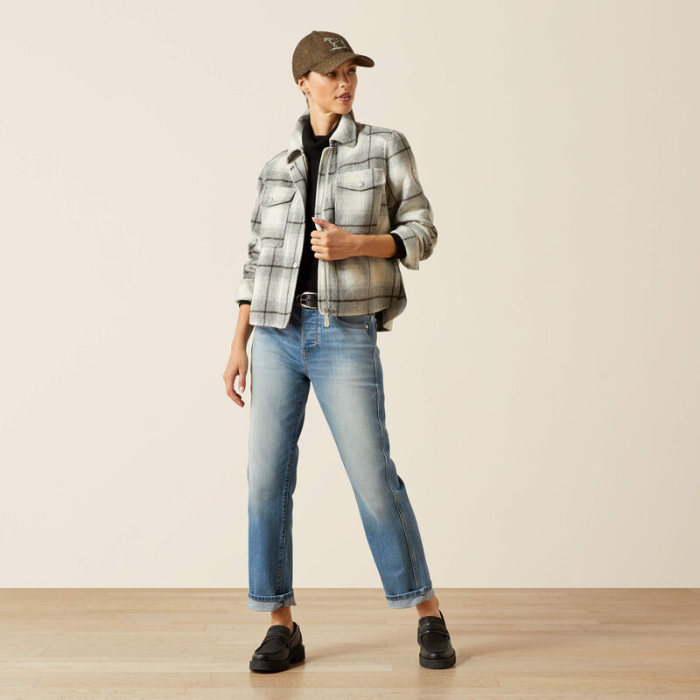 Person wearing a plaid shirt, jeans, and a cap on a plain background