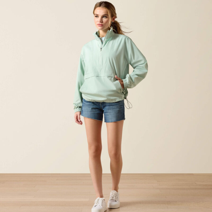 Woman wearing a light green jacket and denim shorts on a plain background