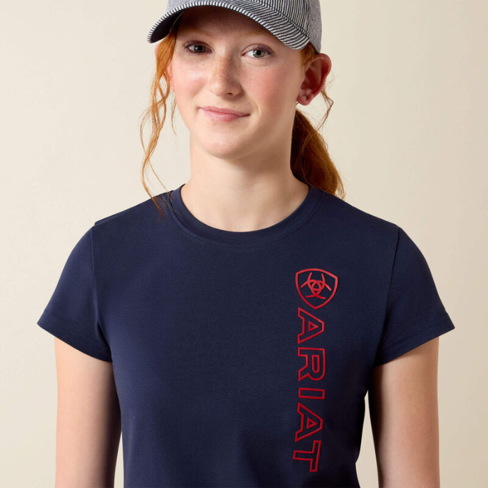 Girl wears navy blue t-shirt with red ARIAT logo on a beige background