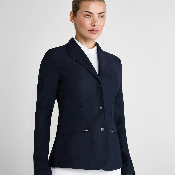 Woman wearing a smart navy jacket and white breeches on a light grey background