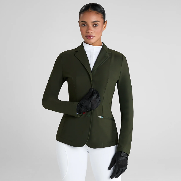Woman wearing a green equestrian jacket and white breeches on a light grey background