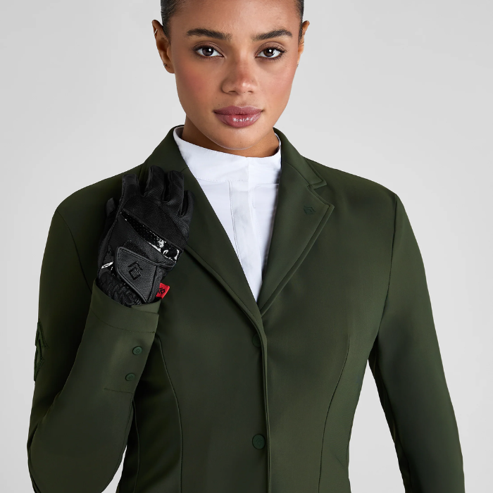 Woman wearing a green coat with a white shirt and black gloves on a light grey background