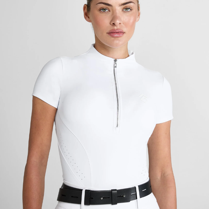 Woman wearing a white equestrian base layer and breeches with a black belt on a light grey background