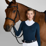 Horse rider stands with horse wearing a blue sweater and white shirt on a grey background