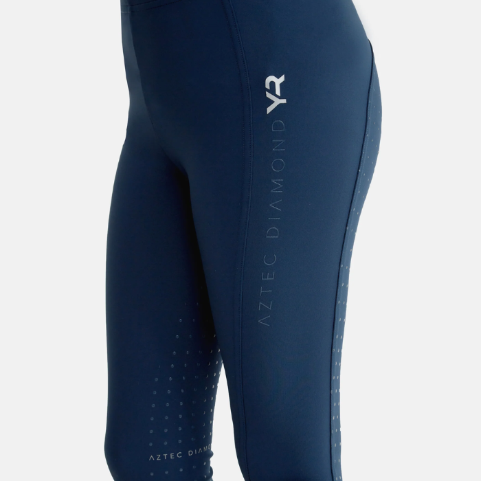 Close up of Aztec Diamond logo on navy riding leggings on a grey background