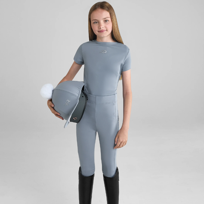 Young rider wears a blue equestrian outfit holding a riding hat on a grey background