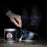 black tin of hoof care been brush on horse hoof,  black background