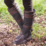 Brown knee-high boots with leather straps worn outdoors on a natural background