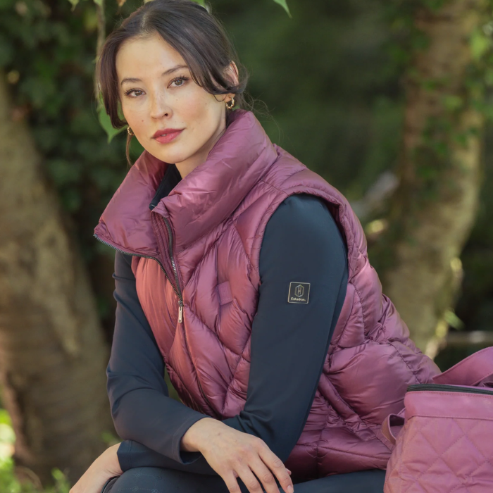 Woman wearing a pink puffer gilet sitting outdoors with greenery in the background