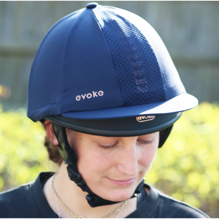 Person wearing a navy equestrian helmet with 'evoke' branding outdoors.