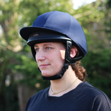 Person wearing a navy riding helmet outdoors with greenery in the background