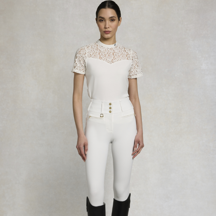 Woman wears a white top with lace collar and white breeches on a grey background