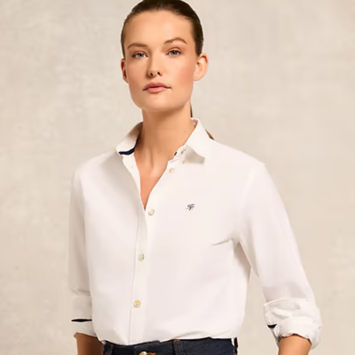Woman wearing a white shirt with a small logo on a beige background
