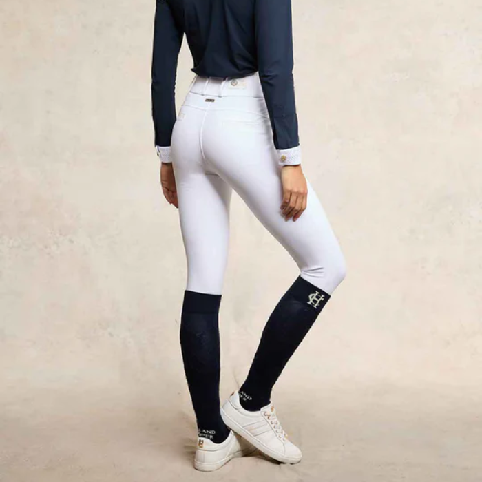 Person wearing white riding breeches with black socks on a beige background