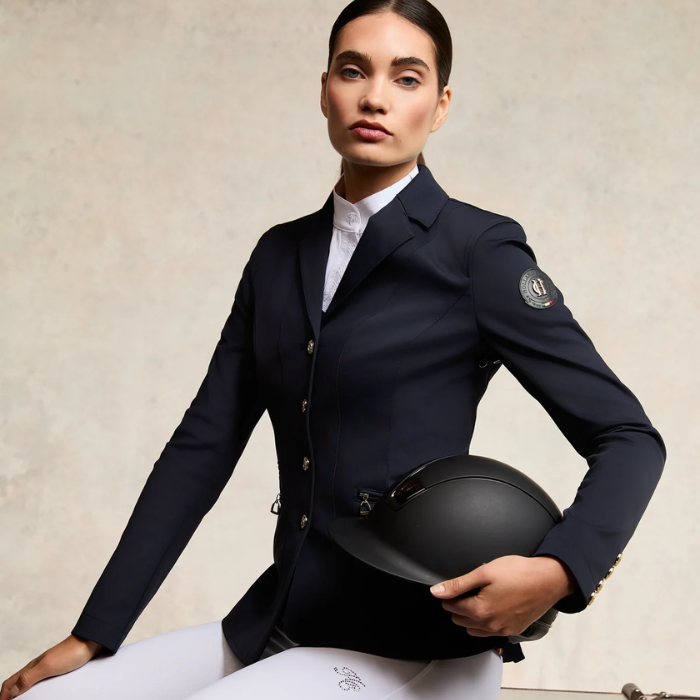 Woman wears a navy equestrian competition jacket on a white background