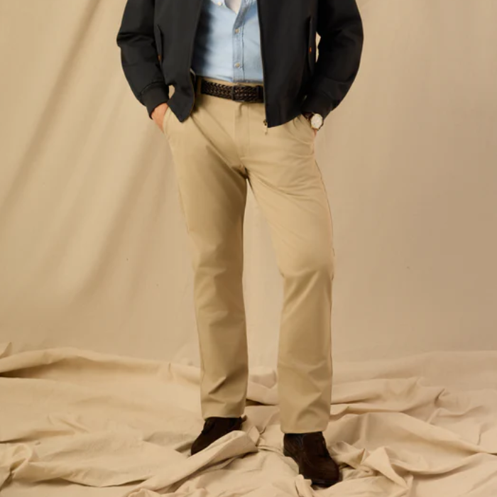 Person wearing a black jacket, light blue shirt, and beige trousers on a beige background