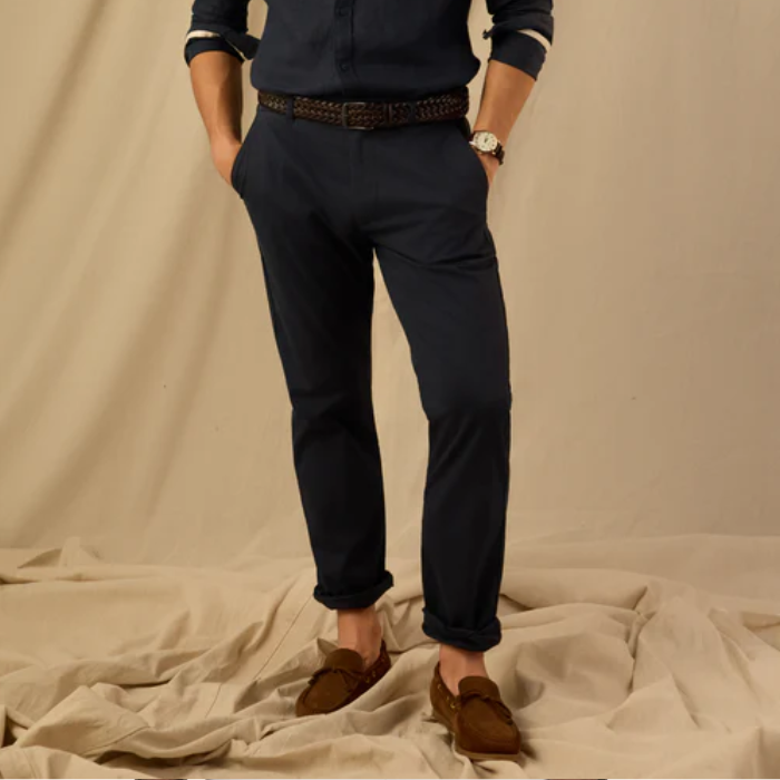 Person wearing navy trousers and brown shoes on a beige background