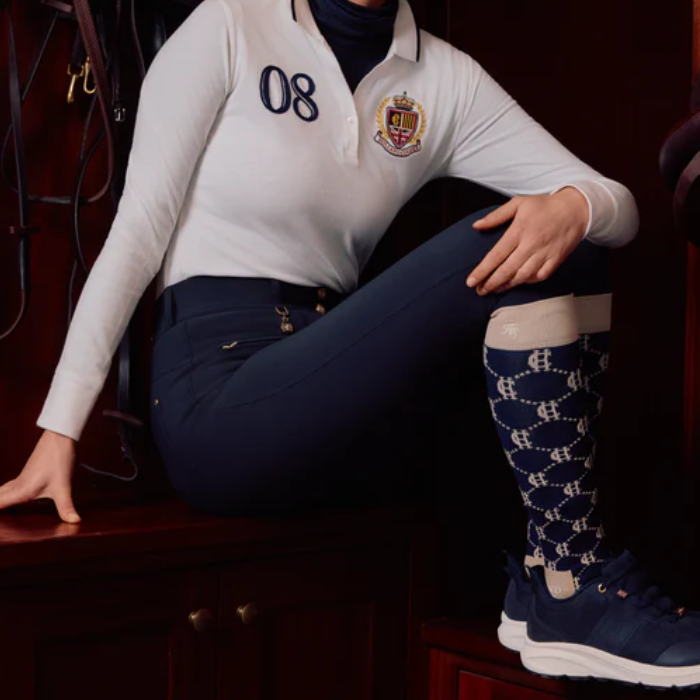 Person wears long riding socks with navy trainers on a dark background