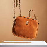 Brown leather handbag with gold chain strap on a beige background