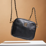 Black handbag with gold chain strap on a beige background