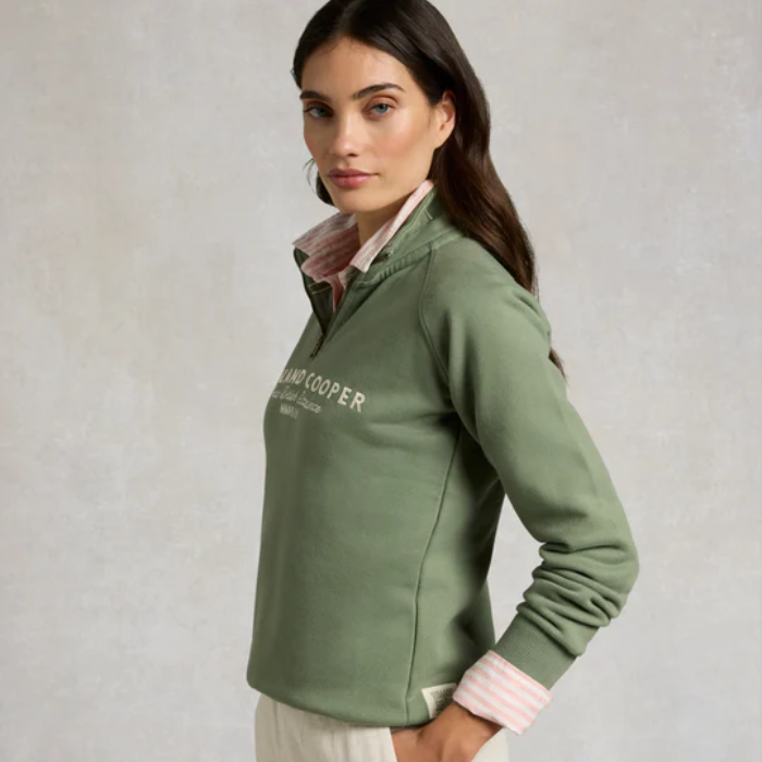 Woman wearing a green jacket with 'Hardy Cooper' branding on a light gray background