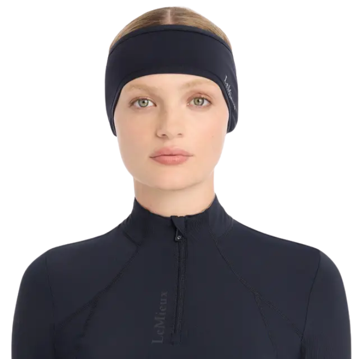LeMieux AW26 Ear Warmer Headband Variant Colour Indigo. A model wearing a blue headband with hair tied back and matching blue top on white background. 