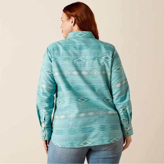 Woman wearing a teal patterned shirt against a beige background