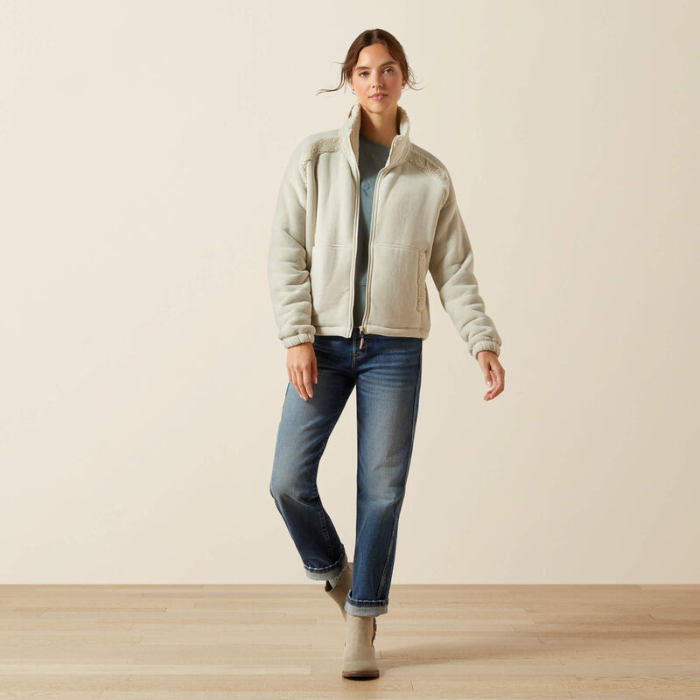 Woman wearing a beige fleece jacket and blue jeans on a plain background