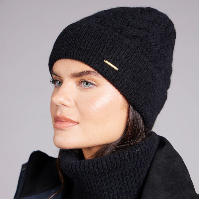 Woman wearing a black knit beanie with a brand logo on a grey background