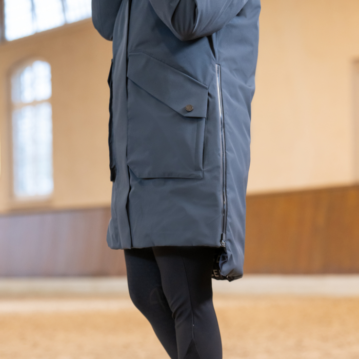 Person wearing a blue jacket in an indoor setting with sand surface and a neutral wall.