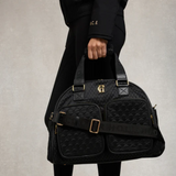 Person holding a black quilted bag with gold accents on a neutral background