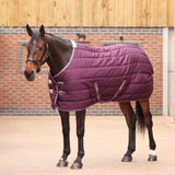 Horse wearing a burgundy quilted rug standing in front of a brick wall.